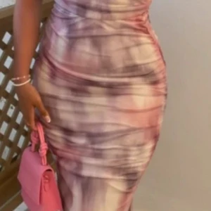 Långklänning i rosa och lila mönster - Supersnygg långklänning med tight passform och slits bak. Klänningen har ett unikt mönster i rosa, lila och beige toner och är tillverkad i ett stretchigt material som sitter perfekt. Perfekt för dig som vill sticka ut med en cool och modern look.