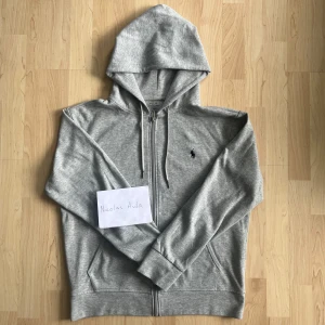 Zip Hoodie Ralph Lauren - Snygg grå hoodie från Polo Ralph Lauren med dragkedja framtill och klassisk huva. Tröjan sitter lite större och passar därför också M. Hör av er i PM om ni har funderingar eller vill ha fler bilder.