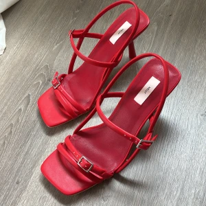 Röda klackar  - Snygga röda klackar från Nelly med smala remmar och fyrkantig tå. Skorna har en elegant hög klack och justerbara spännen vid ankeln. Perfekta för dig som vill sticka ut med en färgstark look. Helt oanvända ✨