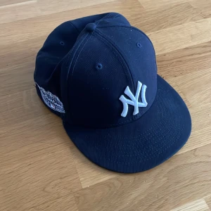 New Era Yankees 59FIFTY keps marinblå - Snygg marinblå New York Yankees 59FIFTY keps från New Era med broderad vit NY-logga framtill och officiella MLB-märken på sidan och bak. Klassisk flat peak och strukturerad passform. Perfekt för dig som gillar streetstyle och sport. Den är köp på JD för 400kr.