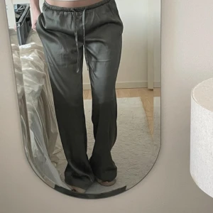 Satinbyxor  - Snygga khakki/gröna satinpants från Bikbok i storlek S. Byxorna har en loose fit med raka ben och elastisk midja med snörning. Materialet är glansigt och mjukt, vilket ger en chill och trendig vibe. Perfekta för dig som gillar bekväma men stilrena byxor.