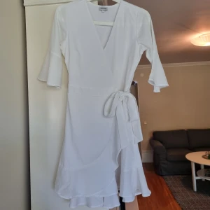Vit omlottklänning från Bubbleroom - Vit omlottklänning från Bubbleroom med volangkant nertill och knyt i midjan. Klänningen har trekvartsärmar med lätt utsvängd ärmslut och v-ringad hals. Klänningen är använd mycket sparsamt och är i mycket gott skick. Perfekt till student eller konfirmation. Skriv för fler bilder eller frågor😊