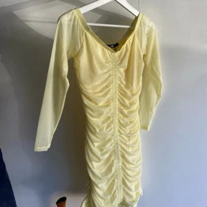Ljusgul från Bik Bok - Supersöt ljusgul kortklänning från Bik Bok med långa ärmar och snygg rynkdetalj framtill. Klänningen har omlottkänsla, volangkant nertill och är gjord i ett tunt, lätt material som känns perfekt för vår och sommar.