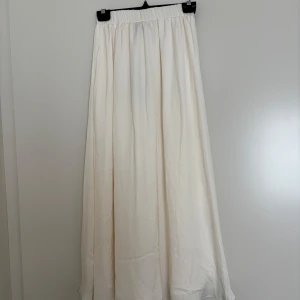 Vit långkjol från Gina Tricot XS - Säljer en flowy och stilren vit långkjol från Gina Tricot i storlek XS. Kjolen har resår i midjan och är tillverkad i ett mjukt, lätt material som ger en snygg siluett. Perfekt för dig som gillar en clean och enkel look.