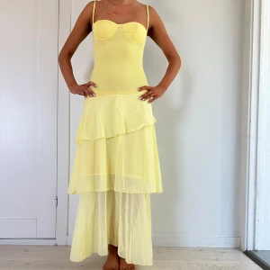 Ljusgul långklänning med volanger - Säljer en ljusgul långklänning med smala axelband och figurnära överdel. Kjolen har flera lager med volanger och är tillverkad i ett lätt, transparent material som ger en luftig känsla. Perfekt för sommarens tillfällen!