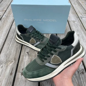 Gröna sneakers från Philippe Model - Säljer ett par snygga gröna Philippe Model sneakers med vita och grå detaljer. Skorna har snörning, rund tå och platt sula. Materialmix av mocka, skinn och syntet ger en exklusiv känsla. Perfekta för dig som gillar stilrena och trendiga sneakers. Nypris på dessa är 3600kr! Ifall ni vill ha mer bilder eller har frågor är det bara att ställa mvh// Partille closet 