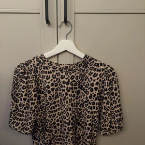 Leopardmönstrad topp med puffärm - Säljer en snygg topp med leopardmönster och puffiga korta ärmar. Toppen har rund halsringning och är i ett mjukt, stretchigt material. Inga defekter. Perfekt för dig som vill sticka ut lite extra! 