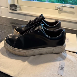 Svarta sneakers från Eytys - Svarta sneakers från Eytys med vit platt sula och lila detalj baktill. Skorna har snörning och är tillverkade i skinn. Perfekta för dig som gillar stilrena och exklusiva sneakers.