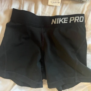 Svarta Nike Pro shorts - Svarta Nike Pro shorts med bred resår i midjan och logga framtill. Tight passform och korta ben, perfekta för träning eller sport. Tillverkade i ett stretchigt syntetmaterial som andas.