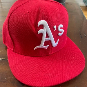 Röd keps från New Era 59FIFTY A's - Röd keps från New Era 59FIFTY med vit broderad A's-logga framtill. Klassisk modell med platt skärm och strukturerad passform. Märkt med storlek 7 1/8 (56,8 cm) på insidan . endast testad!