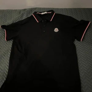 Svart moncler piké - Säljer en svart pikétröja från Moncler. Helt oanvänd då jag tyvärr köpte den i fel storlek. Pris kan diskuteras och är öppen till byten.