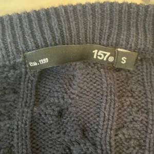 Mörkblå kabelstickad tröja från 157 - Mörkblå kabelstickad tröja från 157 i storlek S. Tröjan har rund halsringning och ribbade muddar vid ärmslut och nederkant. Perfekt för lager-på-lager och passar till många olika stilar.