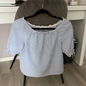 Blårandig blus med knyt på ärmarna - Söt blus med blå och vita ränder, offshoulder-modell och knytband på ärmarna. Blusen har en lös passform och resår vid halsringningen för en bekväm känsla.💓