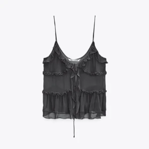 Svart volangtop från zara - Säljer en svart linnetopp med tunna axelband och flera volangdetaljer. Toppen har en v-ringad halsringning och knyt framtill, vilket ger en romantisk och luftig känsla. Perfekt för varma dagar eller lager på lager.