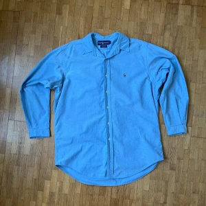 Ljusblå skjorta från Ralph Lauren - Säljer en klassisk ljusblå skjorta från Ralph Lauren i 100% bomull. Skjortan har lång ärm, knappar framtill och den ikoniska broderade loggan på bröstet. Perfekt för en stilren look och enkel att matcha med jeans eller chinos.