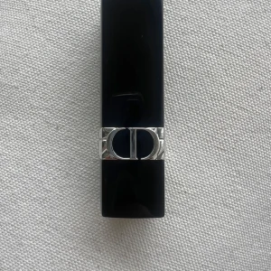 Dior Rouge Dior 999 Metallic Läppstift - Säljer ett lyxigt Rouge Dior 999 Metallic läppstift i en klassisk röd nyans med metallisk finish. Hylsan är svart med silverdetaljer och CD-logga. Perfekt för dig som vill ha en statement-färg på läpparna.  Kommer utan förpackning, oanvänd och otestad, om du köper fler av dessa läppstift kan jag tänka mig bättre pris. Rensning inför flytt. Vissa märken på själva skalet på läppstiftet kan förekomma då jag förvarat alla i samma låda 