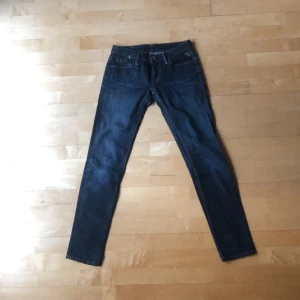 Mörkblå jeansbyxor från Replay - Säljer ett par mörkblå jeansbyxor från Replay med klassisk femficksdesign och snygga kontrastsömmar. Byxorna har normal passform och raka ben, perfekt för en stilren look. Märkespatch bak i midjan och diskret broderad bakficka. XS/34/6