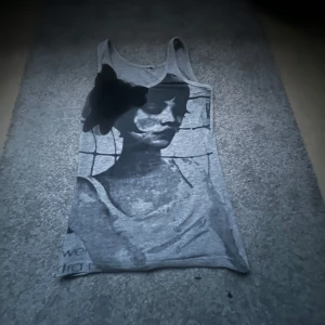 Grått linnetopp med tryck - Säljer ett grått linnetopp med ett stort svartvitt tryck av ett ansikte på framsidan. Toppen har ärmlös design och rund halsringning. Perfekt till sommaren, storleken är mellan S-M men passar även XS