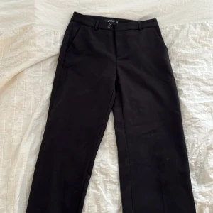 Svarta kostymbyxor från Gina Tricot - Säljer ett par klassiska svarta kostymbyxor från Gina Tricot. Byxorna har normal passform, raka ben och stängs med dragkedja. Jag har också sytt dit en hake då de var för stora för mig i midjan men den behöver man ju inte använda såklart.