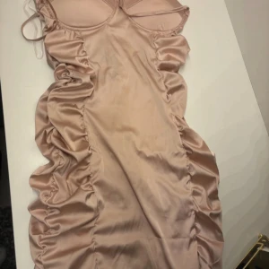 Champagnefärgad tight klänning från Parisian - Säljer en champagnefärgad tight klänning från Parisian med rynkade sidor och tunna axelband. Klänningen har vadderade kupor och en figurnära passform som framhäver siluetten. Perfekt för dig som vill sticka ut!