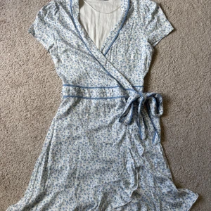 Ljusblå blommig omlott klänning  - Ljusblå blommig sommarklänning med omlott knytning. Perfekt inför sommaren eller midsommar. I storlek S. Som ny. 