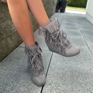 Grå boots med fransar och snörning - Säljer ett par grå boots med snörning och massor av fransdetaljer både framtill och runt skaftet. Skorna har en platt sula och är tillverkade i mockaliknande material. Perfekta för dig som vill sticka ut med din stil!
