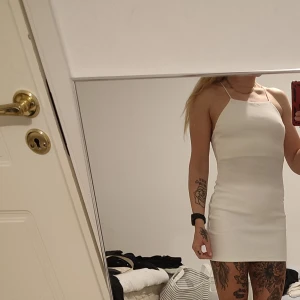 Vit kort klänning med smala axelband - Säljer en stilren vit kortklänning med smala korsade axelband i ryggen och rak halsringning. Klänningen har en tight passform och är perfekt för sommarens alla tillfällen. Enkel och snygg design som framhäver figuren. Använd 1 gång 