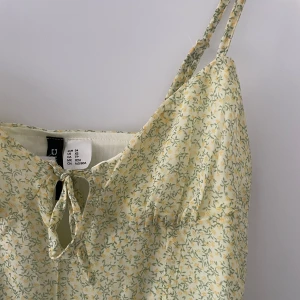 Ljusblommig klänning med knyt framtill - Söt ljus klänning från H&M med smala axelband och blommigt mönster i grönt och gult. Klänningen har en liten knytning framtill och är i en superfin modell som passar perfekt till varma dagar.