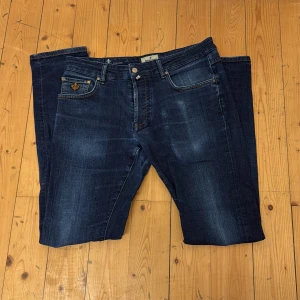 Mörkblå jeansbyxor från Morris - Säljer ett par mörkblå jeansbyxor från Morris, modell Steve Jeans. Klassisk femficksdesign med guldfärgad broderad detalj på myntfickan och snygga kontrastsömmar. Perfekta för dig som gillar stilrena och tidlösa jeans.