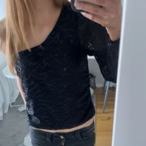 Svart glittrig oneshoulder topp - Säljer en svart glittrig topp med oneshoulder-design och lång ärm. Toppen har ett snyggt glittrande mönster, perfekt för festligare tillfällen!!💗💗