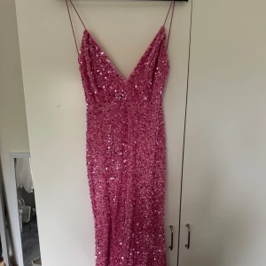 Rosa glittrig långklänning med smala axelband - Säljer en rosa långklänning med smala axelband och v-ringning. Klänningen är täckt av paljetter som ger ett glittrigt intryck och har en figurnära passform. Perfekt för fest eller bal! 💖 Jag hade min på balen, köpte den för 850kr. Skriv för fler bilder, liten fläck på sista bilden☺️ passar även en S