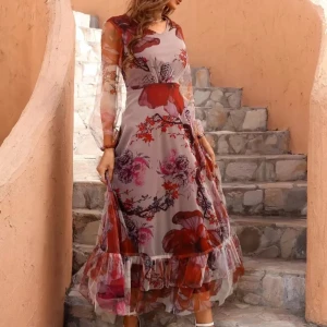 Blommig långklänning med volang - Romantisk långklänning med stora blommor i rött, rosa och lila toner. Klänningen har långärmade transparenta ärmar, v-ringning och volangdetalj nertill. Tillverkad i ett lätt, syntetiskt material som ger ett luftigt intryck.