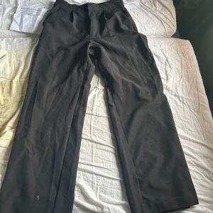Svarta kostymbyxor med raka ben - Svarta kostymbyxor med klassisk passform och raka ben. Byxorna har hög midja och är tillverkade i ett mjukt material som ger en stilren look. Perfekta för dig som gillar en tidlös och enkel stil.aldrig använda 