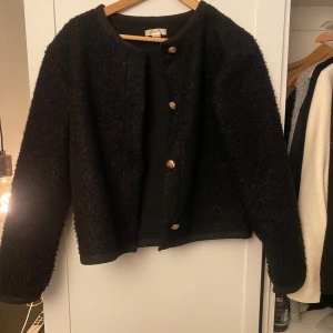 Svart cardigan jacka från Gina Tricot - Säljer en svart cardigan jacka från Gina Tricot med guldiga knappar framtill. Jackan har lång ärm och en mjuk, lite fluffig textur. Den passar mig som oftast har xs eller s💕