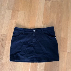 Svart jeanskjol från Only - Säljer en svart jeanskjol från Only med klassisk femficksdesign och knapp framtill. Kjolen är kort och har en rak passform, perfekt till många olika stilar. Enkel och stilren modell som är lätt att matcha. Den har tappat färgen på knappen där fram. 