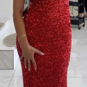 Röd glittrig offshoulder långklänning - Säljer en röd långklänning med glittriga paljetter och offshoulder-modell. Klänningen har en figurnära passform och är perfekt för festliga tillfällen. Materialet är syntet och paljett, vilket ger en snygg och iögonfallande look.