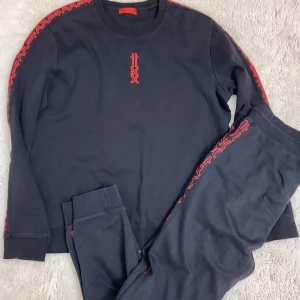 Svart röd Hugo tracksuit. Passar även L - Säljer en svart tröja med röda broderade detaljer längs ärmarna och benen. 