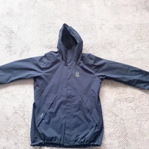 Mörkblå vindjacka från Haglöfs - Säljer en stilren mörkblå vindjacka från Haglöfs. Jackan har en praktisk huva och dragkedja framtill. Använt den endast ett fårtal gånger då jag fick den i vintras. Perfekt nu inför våren, hör bara av er vid några frågor. Nypris 2100