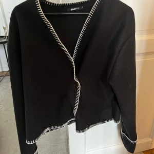 Svart kofta från Gina Tricot - Säljer en svart kofta från Gina Tricot med vita kontrastsömmar längs kanterna. Använd fåtal gånger så nyskick , inga defekter. Storlek s💕
