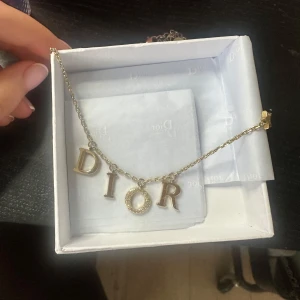 Guldhalsband Dior - Säljer ett elegant guldhalsband från Dior med bokstäverna D, I, O, R. Halsbandet har en stjärndetalj vid låset och kommer i originalförpackning. Perfekt för att ge en lyxig touch till din stil.