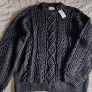 Grå stickad tröja från Vailent  - Säljer en oanvänd snygg grå stickad tröja från Vailent med ett klassiskt flätmönster. Tröjan har långa ärmar och ribbade kanter vid ärmslut och nederkant. Ord. pris 699.