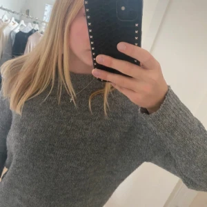 Grå stickad tröja - Säljer en stilren grå stickad tröja med långärmad design. Perfekt för kyligare dagar och enkel att matcha med olika outfits. Tröjan har en klassisk passform och är gjord i ett mjukt material för extra komfort.