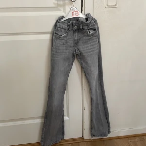 Grå bootcut jeans från H&M - Snygga grå bootcut jeans från H&M med justerbar låg midja. Perfekta för en avslappnad stil med en klassisk look. De har fickor både fram och bak samt en knapp och dragkedja framtill.