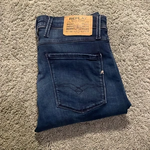 Blå jeans från Replay - Snygga blå jeans från Replay med klassisk femficksdesign och en stilren look. De har en knappgylf och är tillverkade i ett stretchigt material för extra komfort. Perfekta för en avslappnad stil.