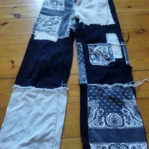 Patchwork byxor med bandanamönster - Unika patchwork byxor med svart och vit design. Byxorna har ett coolt bandanamönster och fransiga kanter för en edgy look. Perfekta för dig som vill sticka ut med en kreativ stil.
