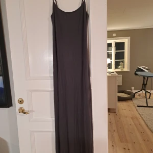 Mörkgrå långklänning med smala axelband - Elegant mörkgrå långklänning från Soft Touch med smala axelband. Perfekt för en stilren och minimalistisk look. Klänningen har en enkel och tidlös design som passar många tillfällen.