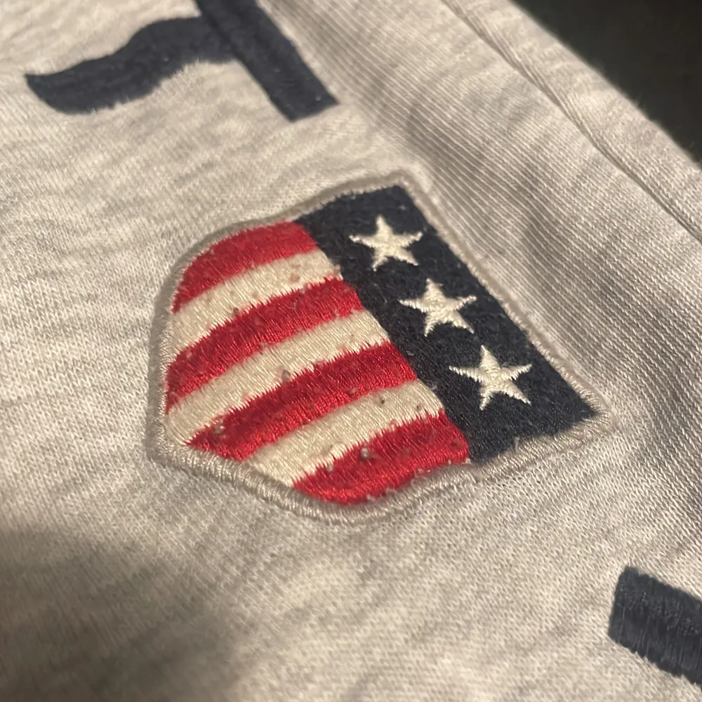 Säljer ett par grå mjukisbyxor från GANT med tryck 'GANT 1949' och ett broderat emblem på benet. Byxorna har snörning i midjan och är perfekta för en avslappnad stil.. Farkut & Housut.