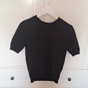 Svart kortärmad tröja - Säljer en stilren svart tröja med korta ärmar. Perfekt för en minimalistisk look. Tröjan har en rund halsringning och är gjord i ett mjukt material.
