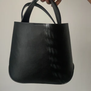 Ginatticot Svart handväska i skinn - Elegant svart handväska i skinn med en stilren design. Perfekt för att bära dina dagliga nödvändigheter med stil. Väskan har två handtag för enkel bärning.