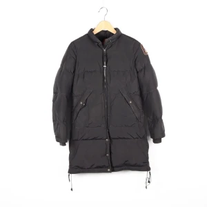 Svart dunjacka från Parajumpers - Säljer en svart dunjacka från Parajumpers, Masterpiece Series. Jackan har en lång design med dragkedja och flera praktiska fickor. Den har en patch på ärmen och justerbara snören i nederkant. Perfekt för kalla vinterdagar.